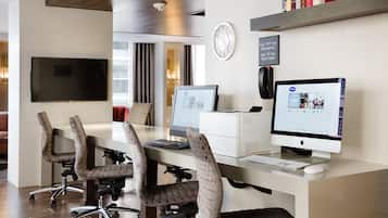 A modern office space with a long desk, multiple chairs, a flat-screen TV, and a computer monitor.