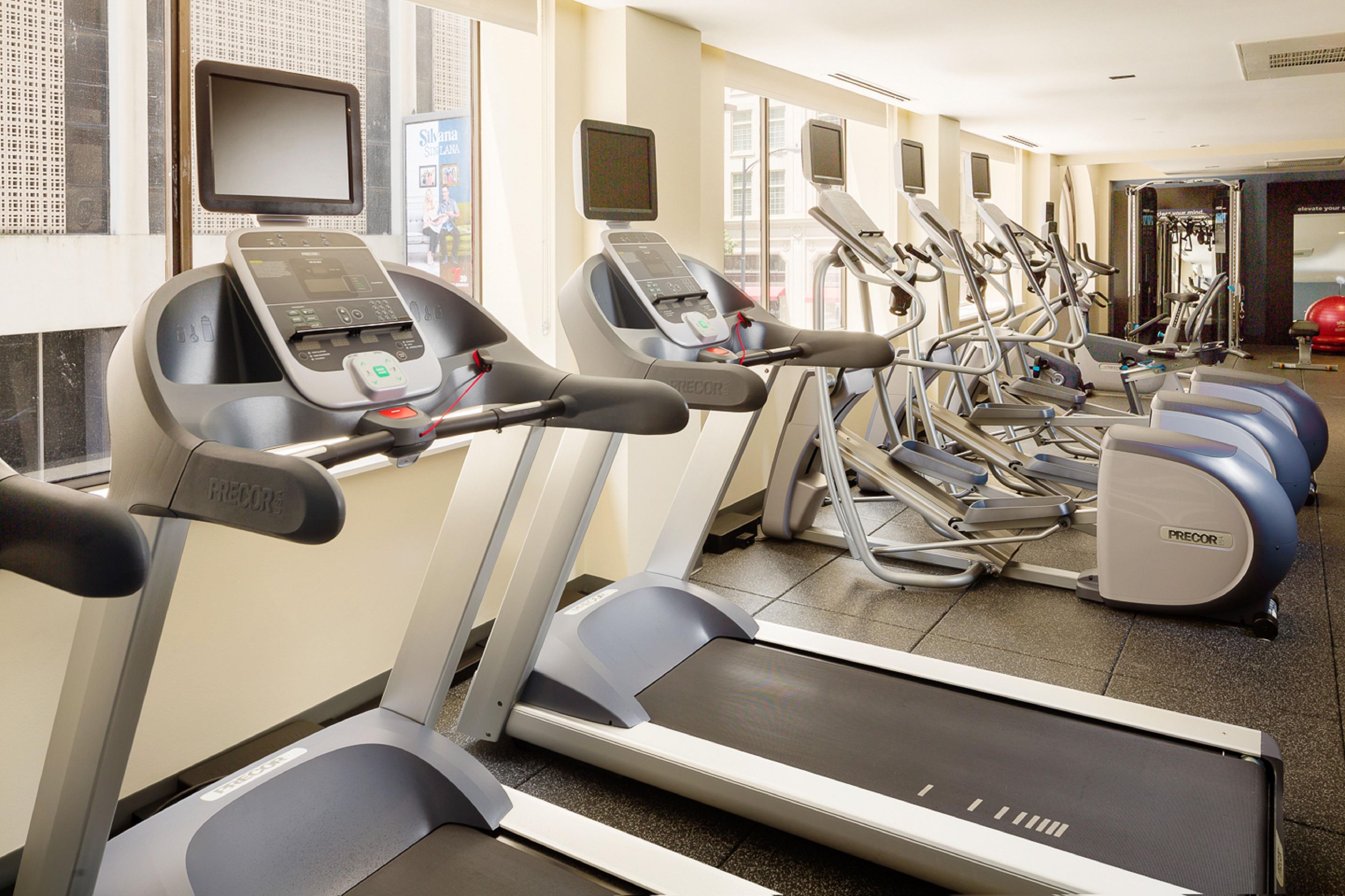 A row of treadmills in a gym with a mirrored wall and a window.