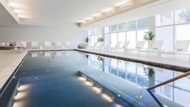 A large indoor swimming pool with clear water, surrounded by white lounge chairs and potted plants. - Hampton Inn & Suites Dallas Downtown (Dallas)