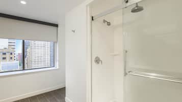 A modern bathroom with a glass shower enclosure, a visible window, and a view of the cityscape.