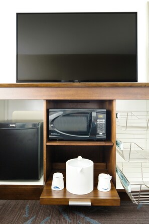A flat-screen TV mounted above a wooden shelf with a microwave and a coffee maker. - Hampton Inn & Suites Dallas Downtown (Dallas)
