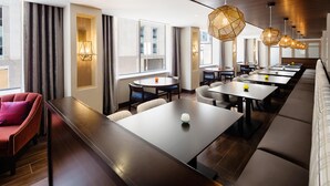 A modern hotel dining area with long tables, cushioned seating, and pendant lighting. - Hampton Inn & Suites Dallas Downtown (Dallas)