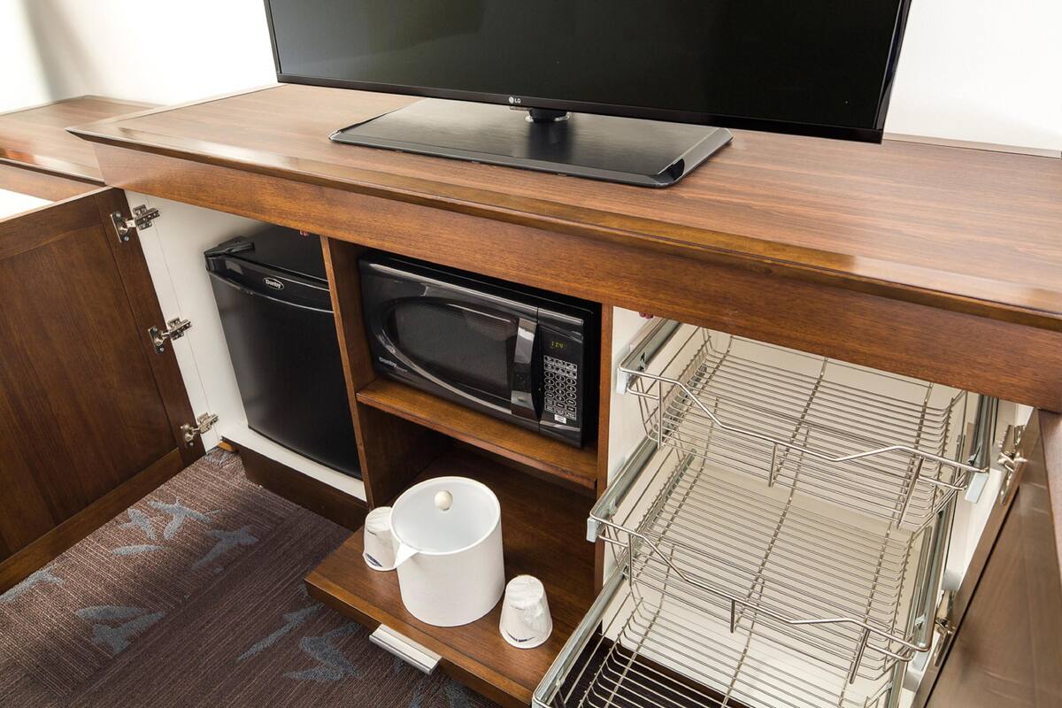 A compact kitchenette with a microwave, a small oven, a coffee maker, and a TV on a wooden countertop.