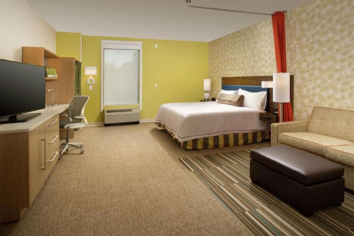 A hotel room with a bed, a sofa, a TV, a desk, and a chair.