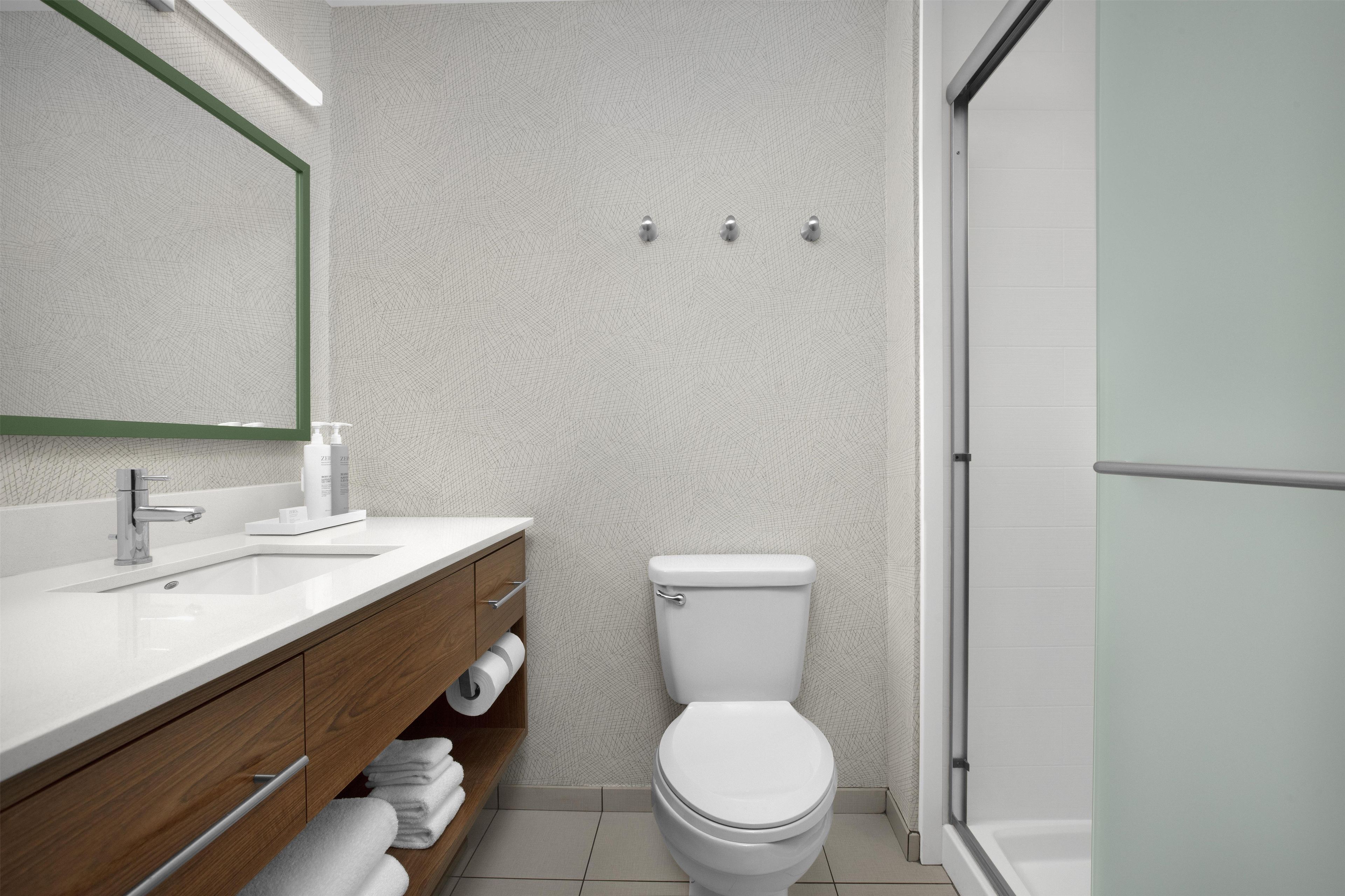 A modern bathroom with a white toilet, a wooden vanity, a mirror, and a shower area.