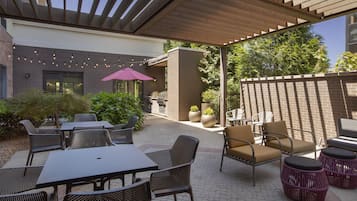 An outdoor patio with tables and chairs, a grill, and potted plants.