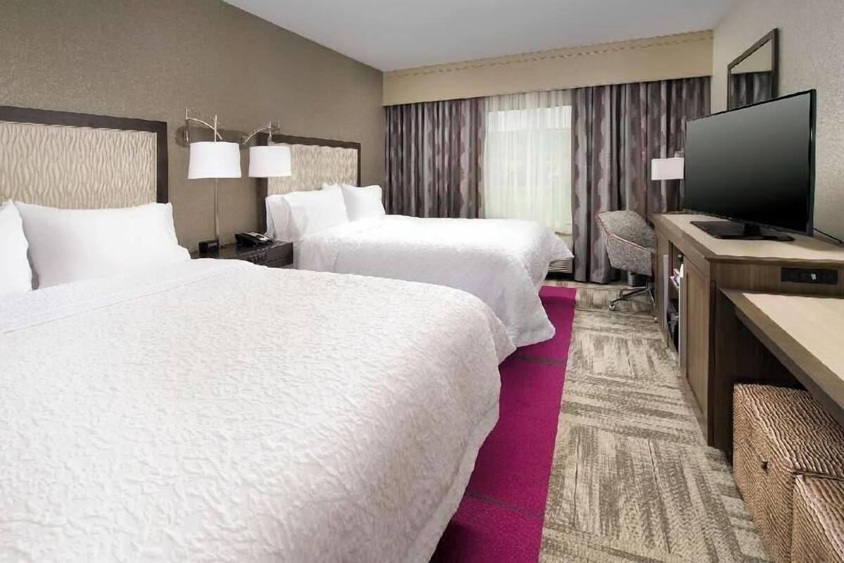 A hotel room with two beds, a desk with a television, and a chair.