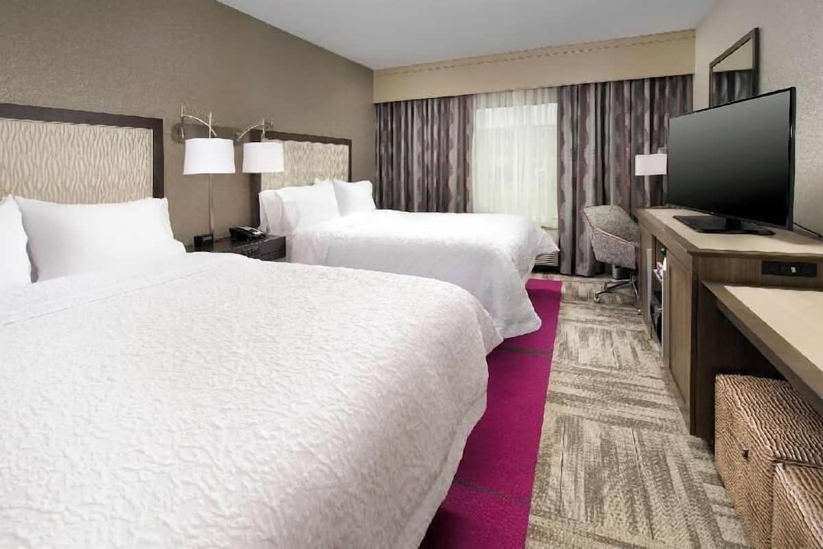 Quarto de hotel com duas camas, uma mesa de trabalho e uma televisão, e uma cadeira.