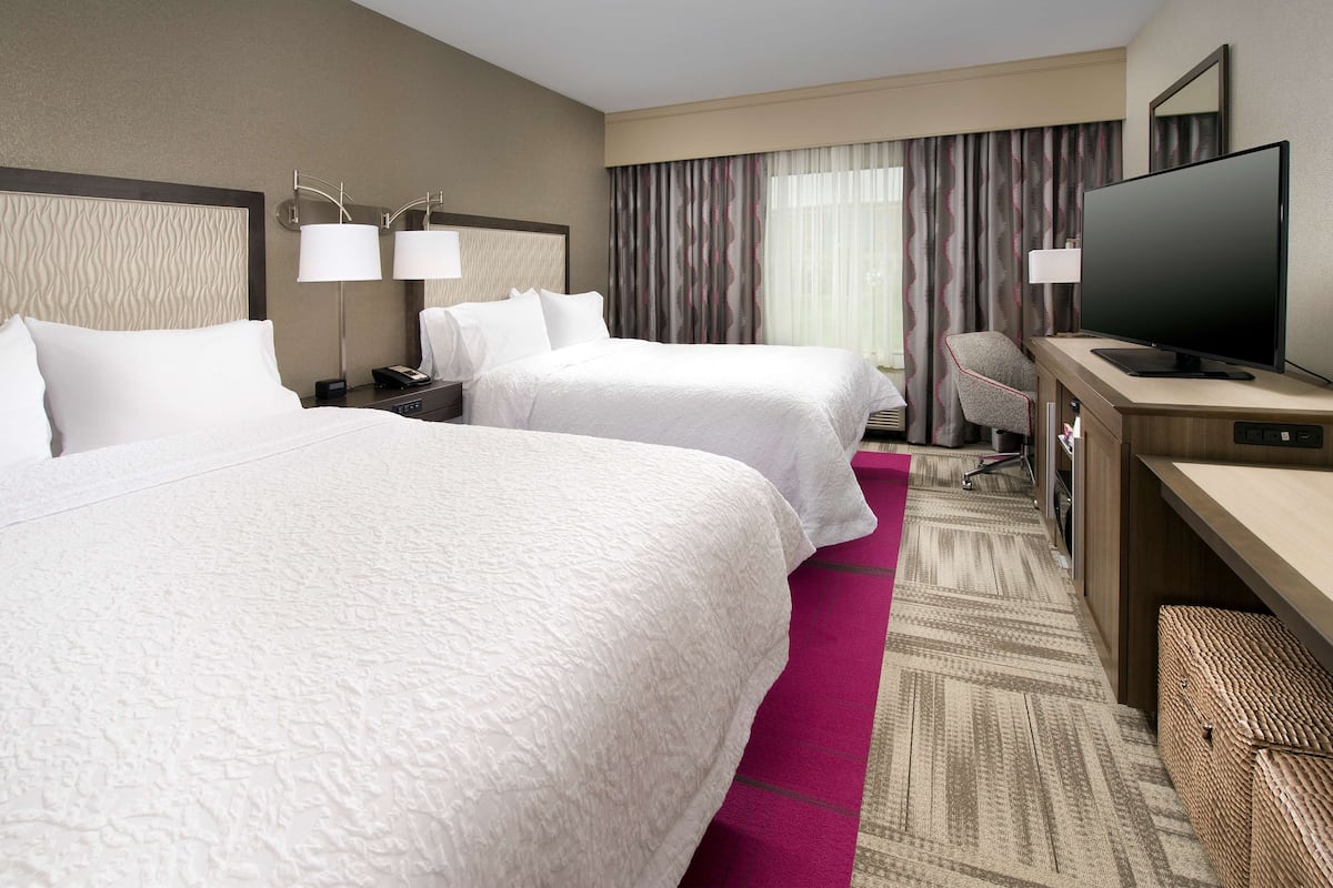 A hotel room with two beds, a desk with a television, and a chair.