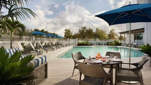 Un espace aménagé au bord de la piscine, avec des chaises longues, des parasols et une table à manger pour deux personnes.