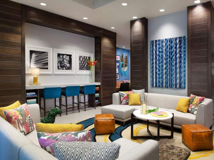 A modern hotel lobby with a sofa set, a coffee table, and a bar area with blue chairs.