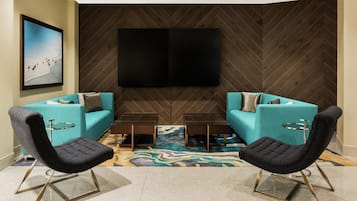 A modern living room with two teal sofas, black chairs, a coffee table, and a large flat-screen TV mounted on a herringbone-patterned wall.