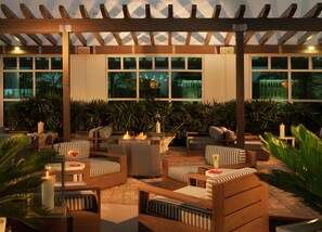 An outdoor seating area with wooden furniture and a fire feature. - Hilton Garden Inn Miami Dolphin Mall (Miami)