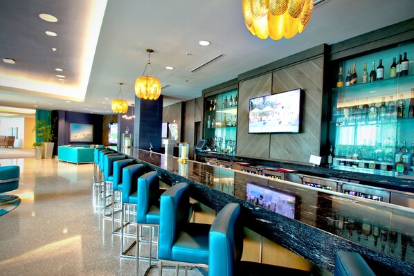 A bar area with a long counter, multiple bar stools, and a television screen.