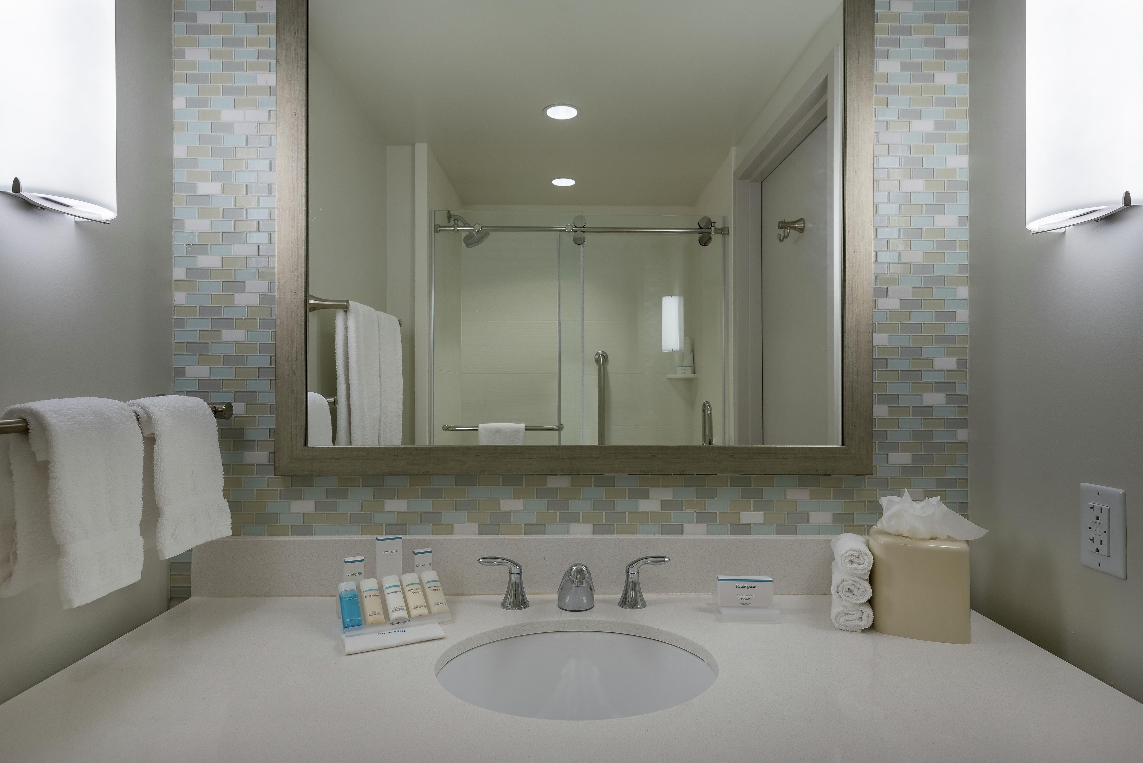 A bathroom with a large mirror, a sink, and a shower.