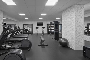 Une salle de sport équipée de tapis de course, d’un banc de musculation, d’un support à squats et de ballons d’exercice.