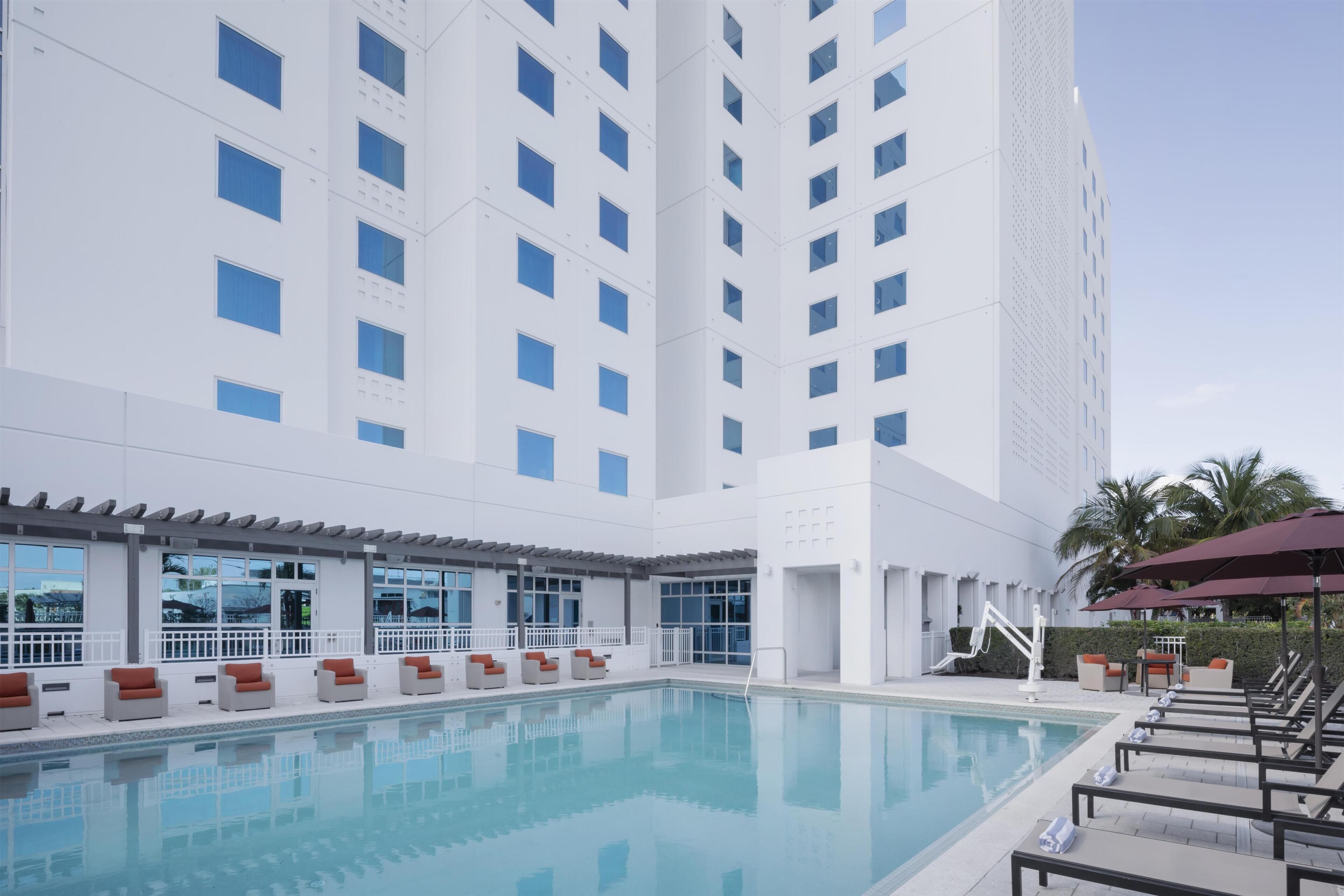 A modern hotel with a swimming pool, outdoor seating, and a tall building in the background.