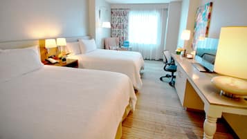 A hotel room with two beds, a desk with a lamp, a chair, a TV, and a window with curtains.