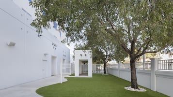 Un edificio moderno con facciata bianca, un prato curato e un albero al centro.