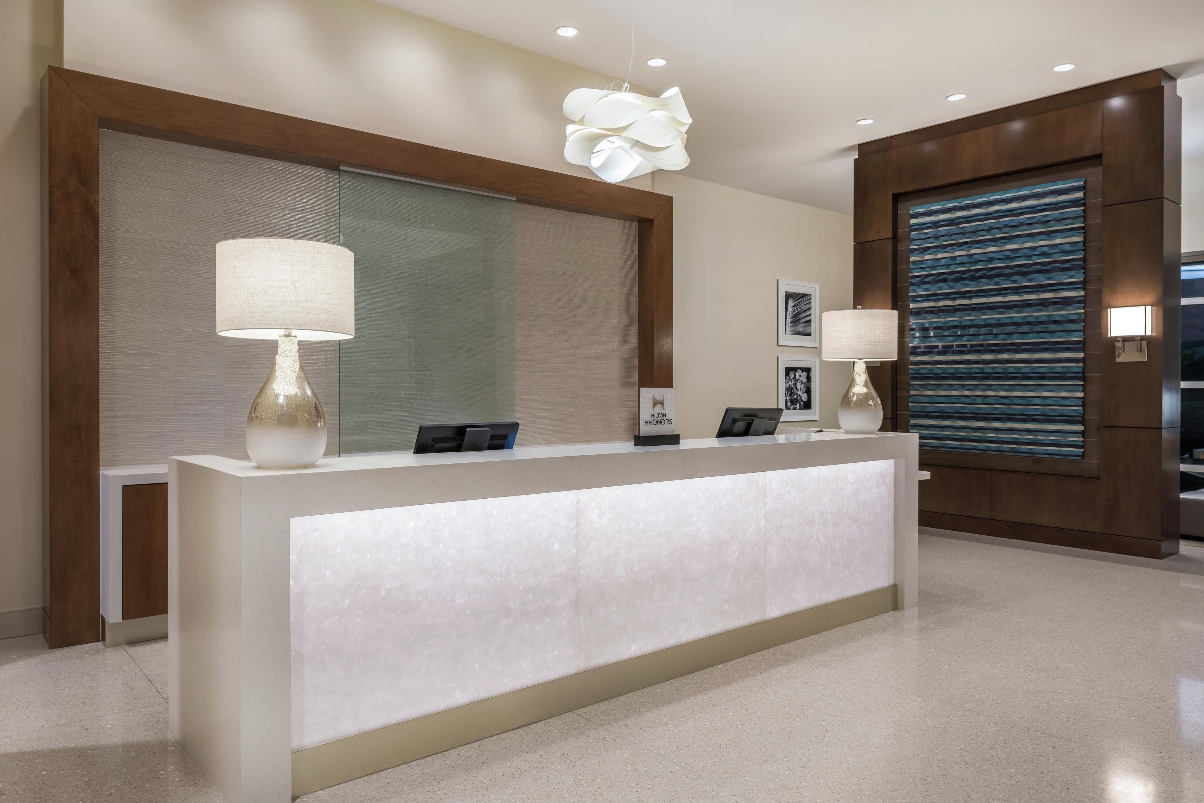 A hotel reception desk with a modern design, featuring a large mirror, two lamps, and a digital display.