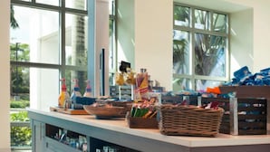 Un espace cuisine doté d’un grand îlot central, de divers ustensiles de cuisine et offrant une vue sur l’extérieur grâce à de grandes fenêtres.