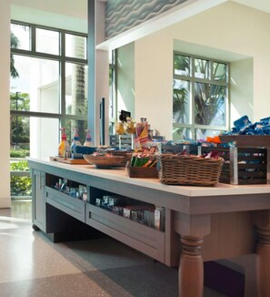A kitchen area with a large island, various kitchen utensils, and a view of the outdoors through large windows. - Hilton Garden Inn Miami Dolphin Mall (Miami)