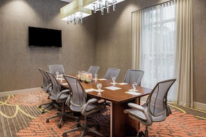 A conference room with a long table, chairs, a flat-screen TV, and a large window with curtains. - Hilton Garden Inn Miami Dolphin Mall (Miami)