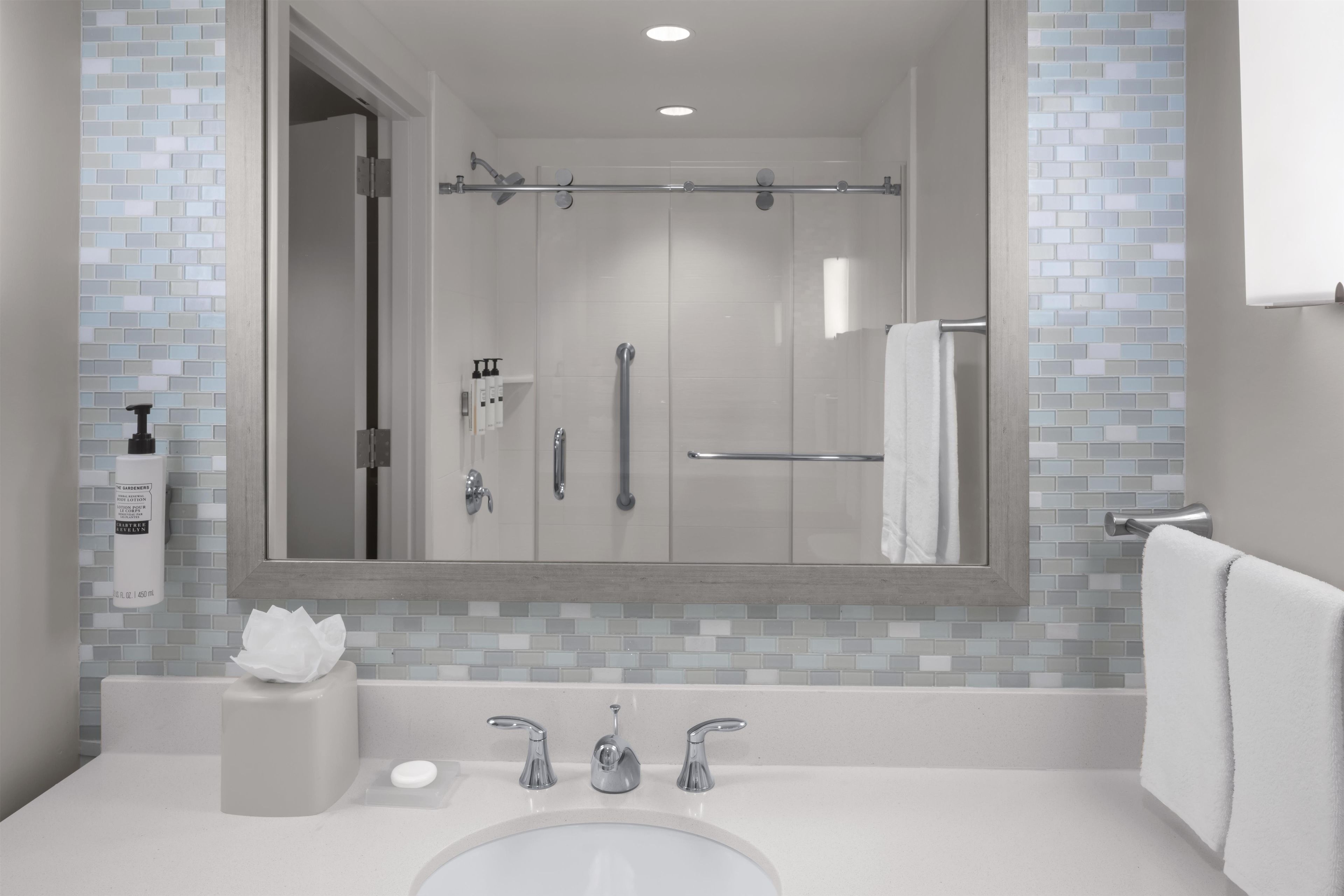 Un baño moderno con cabina de ducha de vidrio, un espejo grande y un lavamanos blanco con dos grifos.