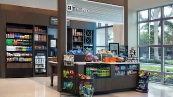 Una tienda de snacks con gran variedad de productos, un refrigerador y vistas al exterior a través de amplios ventanales.