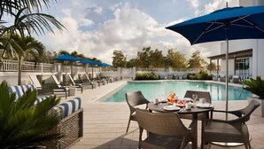 A poolside area with lounge chairs, umbrellas, and a dining table set for breakfast.