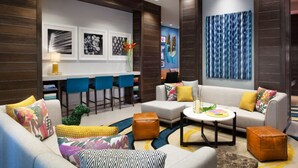 A modern hotel lobby with a sofa set, a coffee table, and a bar area with blue chairs.