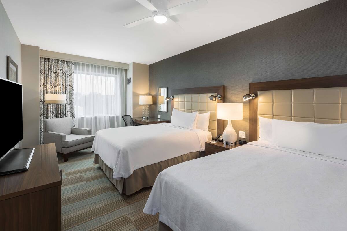 Habitación de hotel con dos camas, un escritorio, una silla, un televisor y un ventilador de techo.