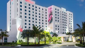 A large hotel with multiple floors, a prominent flamingo mural, and a well-maintained garden with palm trees.