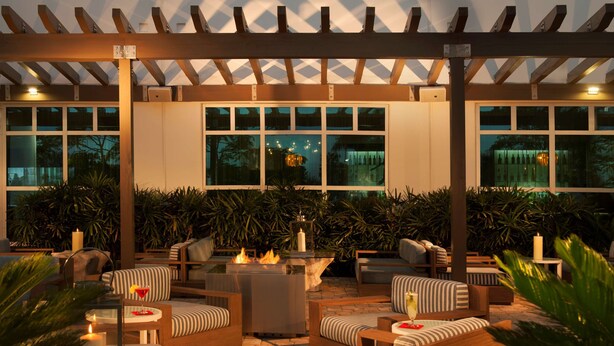An outdoor patio area with seating, a fire feature, and large windows.