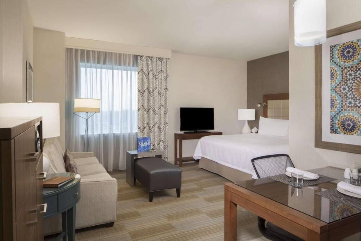 Habitación de hotel con cama, televisor, escritorio, silla, sofá y lámpara.