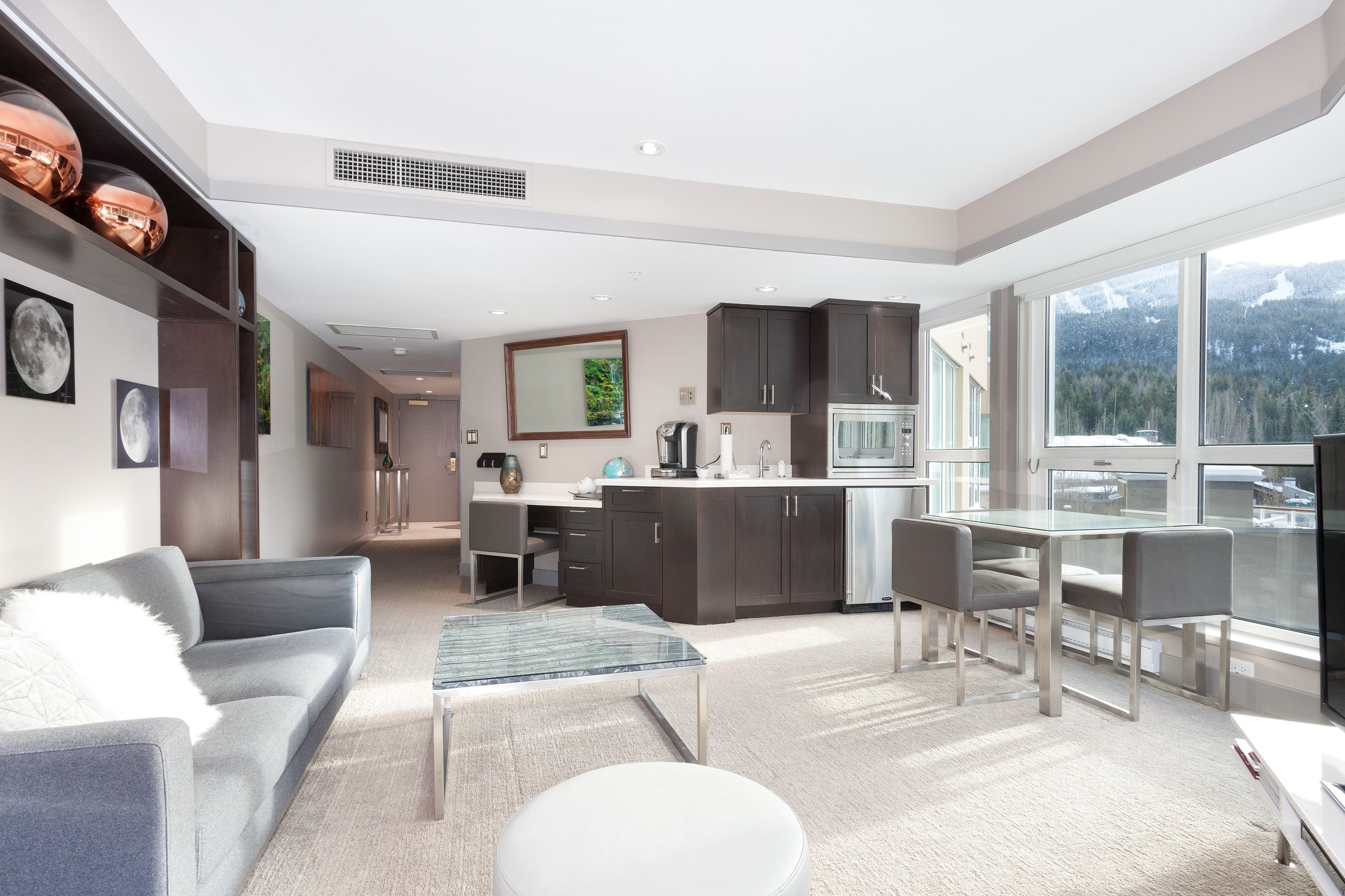 A modern kitchen with dark cabinets, a dining area with a glass table, and a sofa with a white cushion.