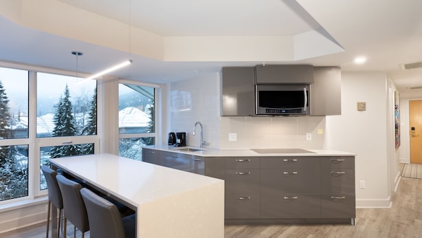 A modern kitchen with a large island, grey cabinets, and a built-in microwave.