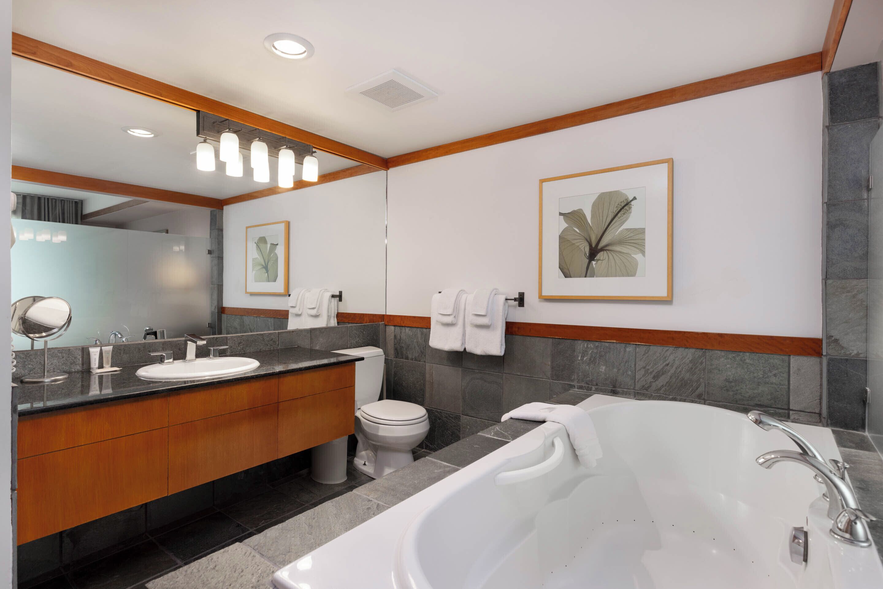 A modern bathroom with a large mirror, a sink, a toilet, and a bathtub.