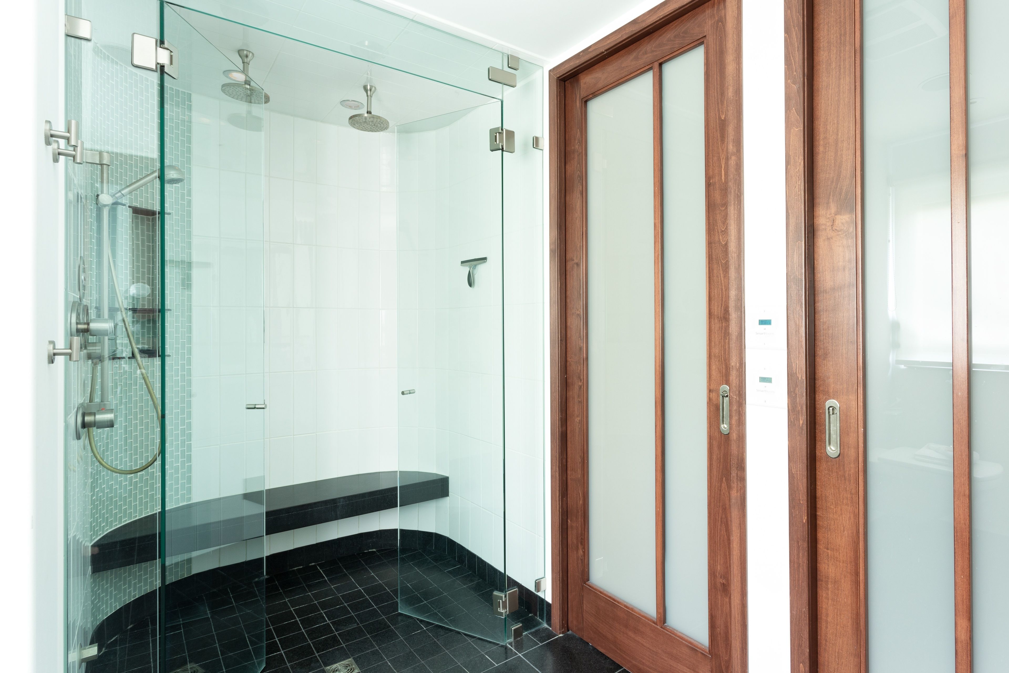 Une salle de bain moderne avec une douche à parois de verre, une porte en bois et un sol carrelé de noir.