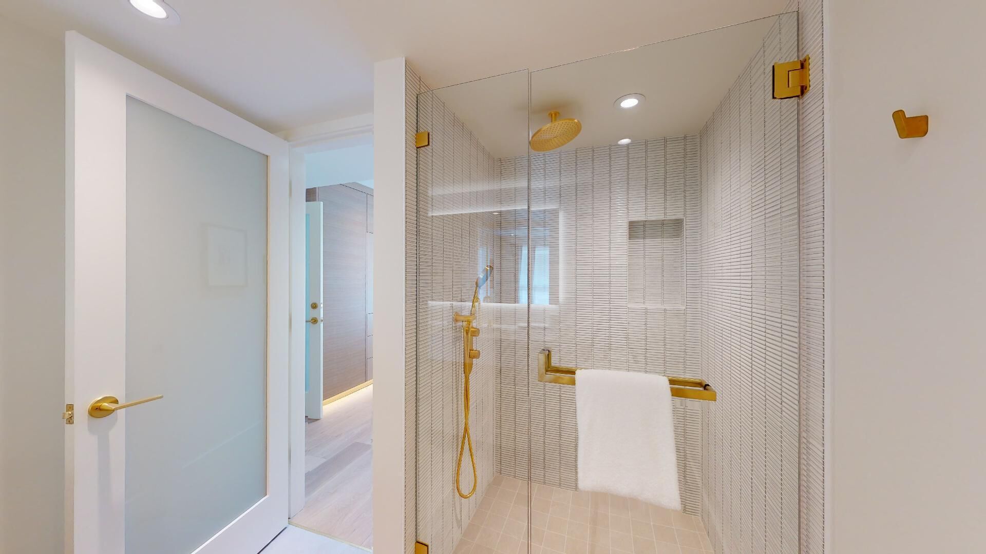 A modern bathroom with a glass-enclosed shower, a towel rack, and a visible door leading to another room.