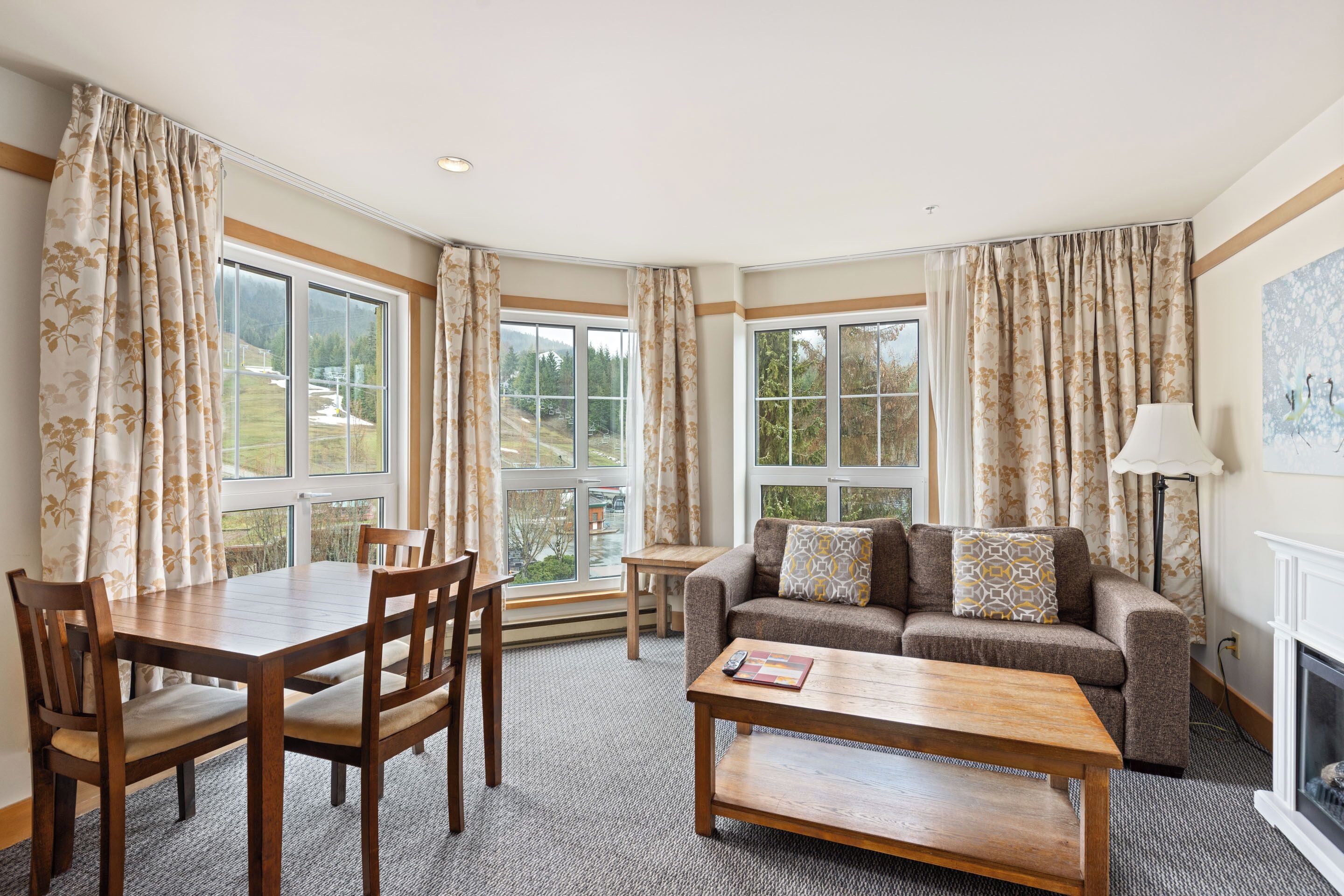 A cozy living room with a wooden dining table, chairs, a sofa with cushions, and a fireplace.