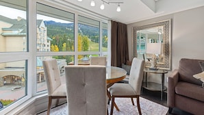 A room with a large window, a round glass table, and four chairs.