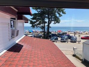 A view of a beachside parking lot with cars and a white building with a red roof. - Grand View Motel (Hampton)