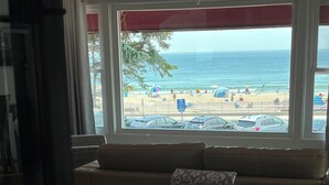 A room with a sofa facing a window overlooking a beach.