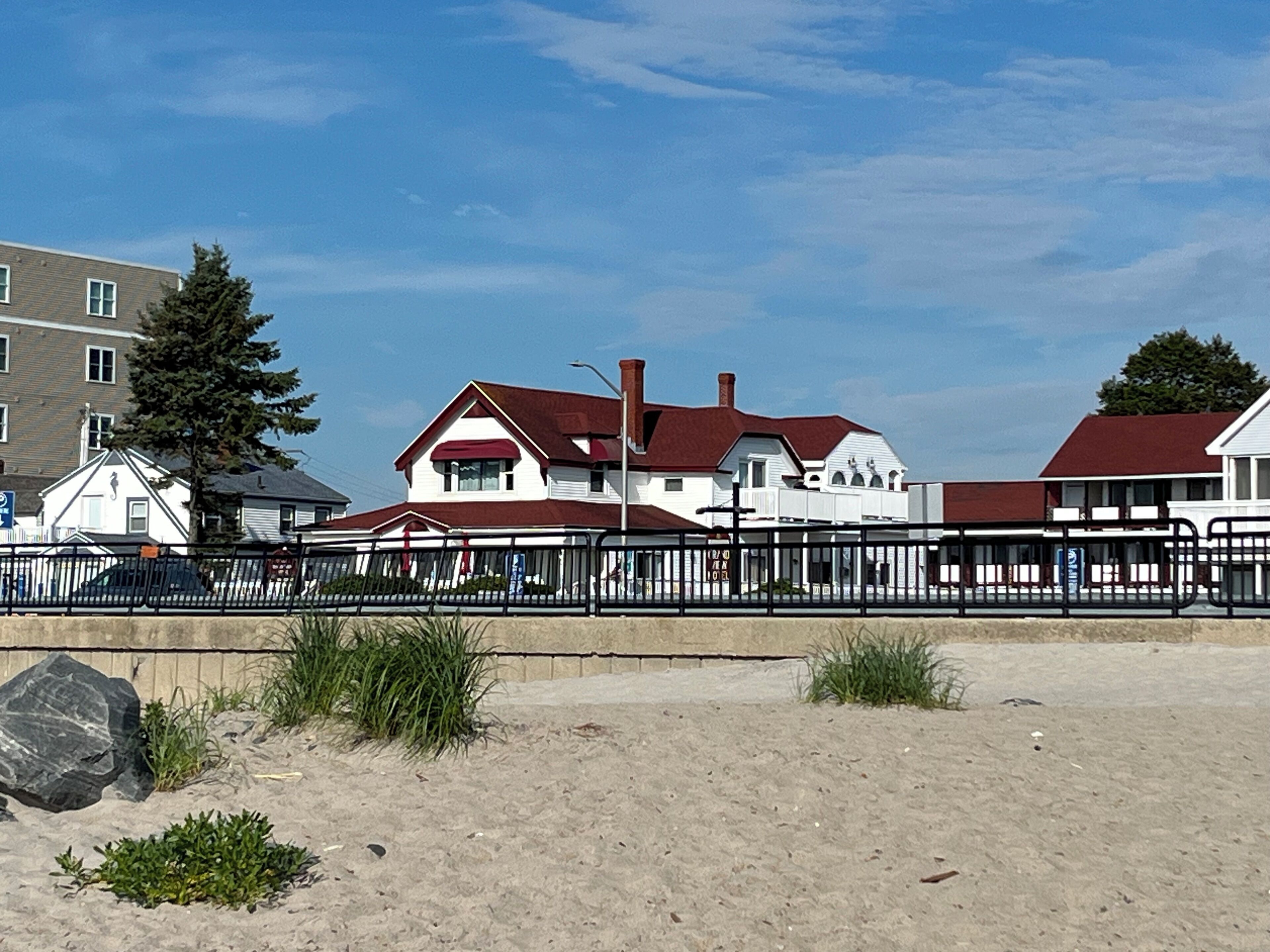 A beachfront property with a sandy beach, a wooden fence, and a red-roofed house.