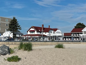 A beachfront property with a sandy beach, a wooden fence, and a red-roofed house.