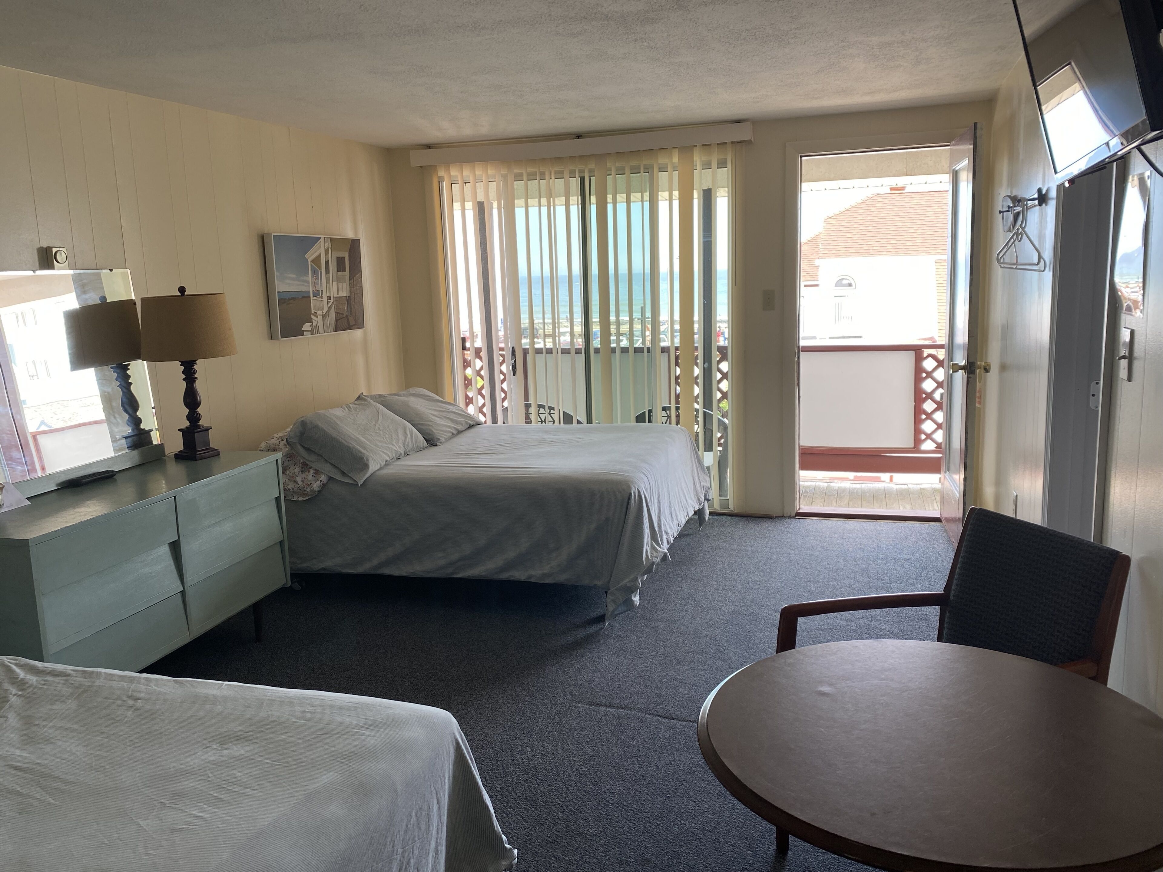 A hotel room with a bed, a desk with a lamp, a chair, and a view of the outside.