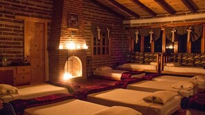 Um quarto rústico com quatro camas dispostas em linha, uma lareira e uma janela com cortinas.