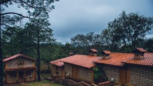 Uma área rústica com várias cabanas de madeira, cada uma com telhado de telhas vermelhas, cercada por árvores.