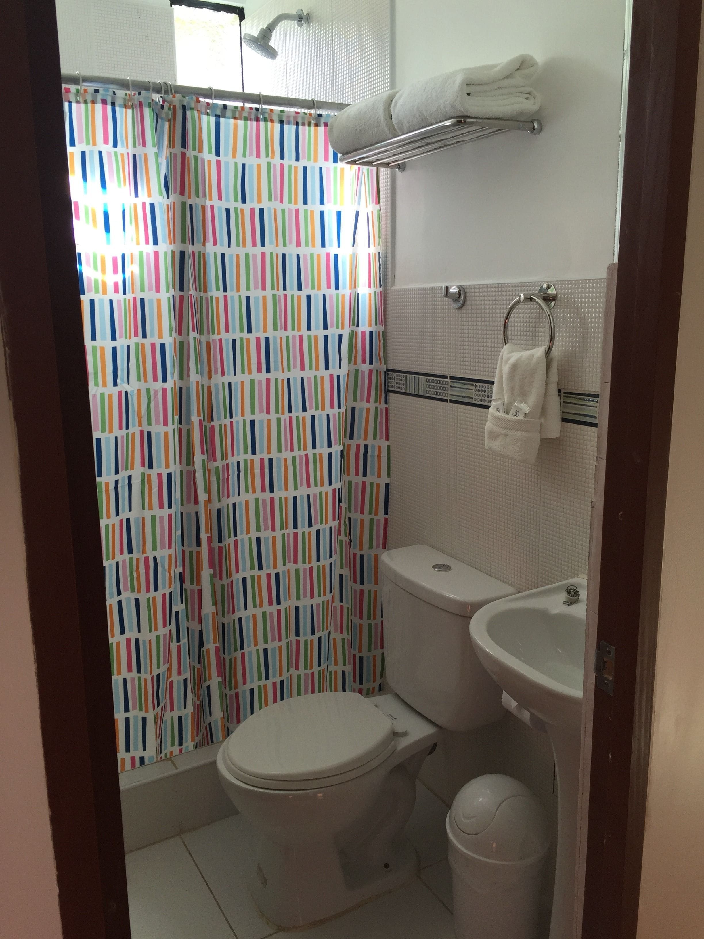 A bathroom with a striped shower curtain, a toilet, a sink, and a towel rack.